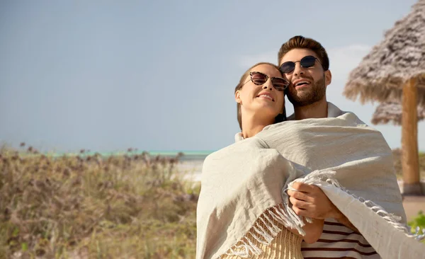 Ευτυχισμένο ζευγάρι καλυμμένο με κουβέρτα αγκαλιάζει στην παραλία — Φωτογραφία Αρχείου