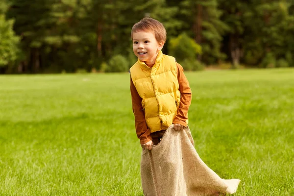 Niño feliz jugando juego de saltos bolsa en el parque —  Fotos de Stock