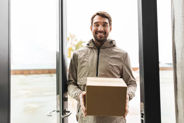 Repartidor sonriente con caja de paquetes a puerta abierta — Foto de Stock