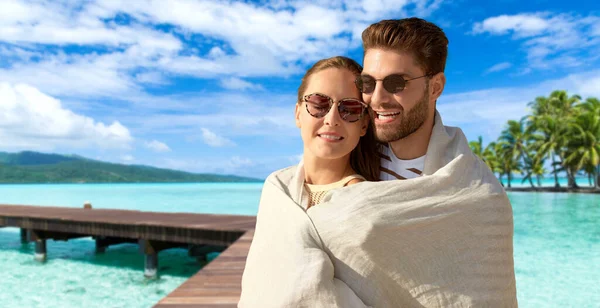 Feliz pareja cubierta con manta abrazos en la playa —  Fotos de Stock