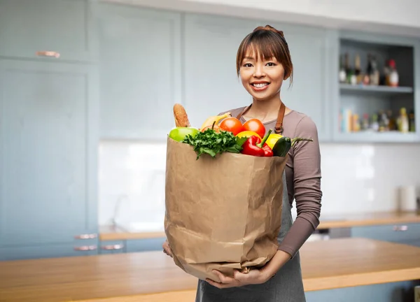 Улыбающаяся женщина с едой в бумажном пакете на кухне — стоковое фото