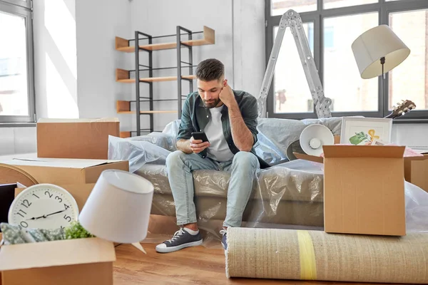 Hombre triste con teléfono inteligente y cajas de mudanza a casa —  Fotos de Stock