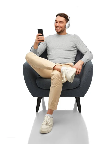 Man with phone and headphones sitting in chair — Stockfoto
