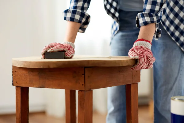 Mulher lixar mesa de madeira redonda velha com esponja — Fotografia de Stock