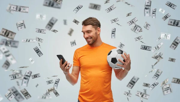Hombre con teléfono inteligente y pelota de fútbol sobre el dinero —  Fotos de Stock