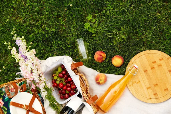 Food, drinks and basket on picnic blanket on grass — Stock Photo, Image