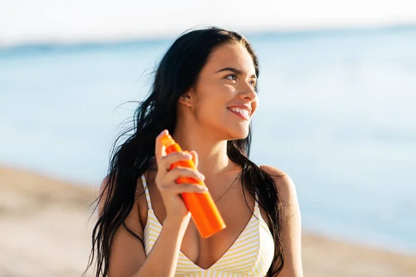 Mujer sonriente en bikini con protector solar en la playa — Foto de Stock