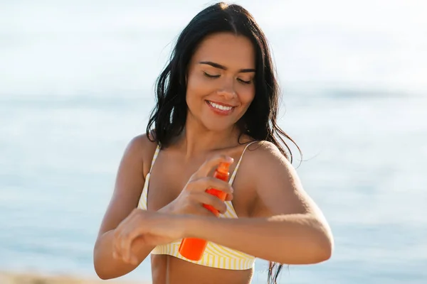 Mujer sonriente en bikini con protector solar en la playa — Foto de Stock