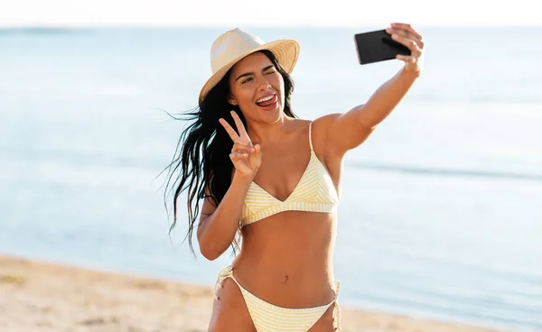 Улыбающаяся женщина в бикини делает селфи на пляже — стоковое фото