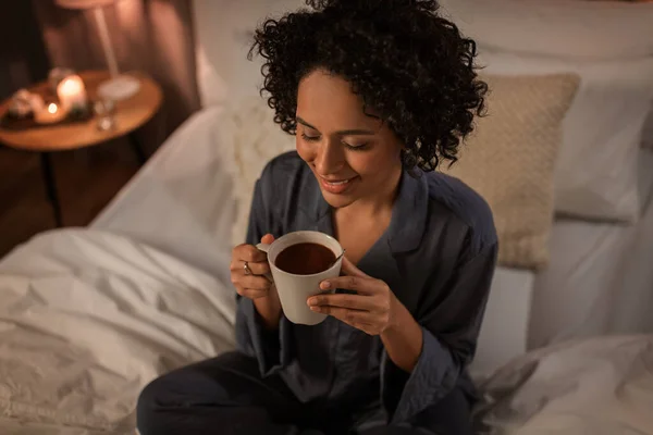 Szczęśliwa kobieta z gorącą czekoladą siedzi w łóżku — Zdjęcie stockowe