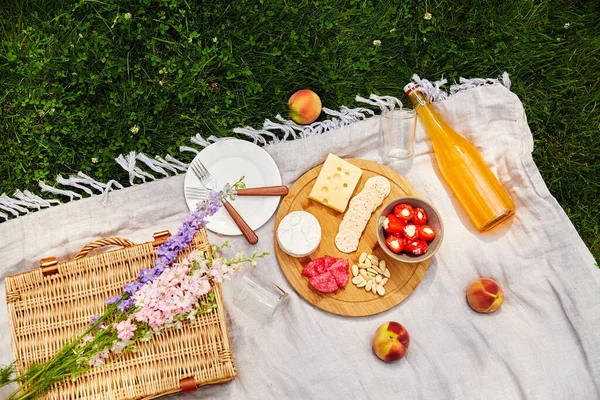 Food, drinks and basket on picnic blanket on grass — Stock Photo, Image