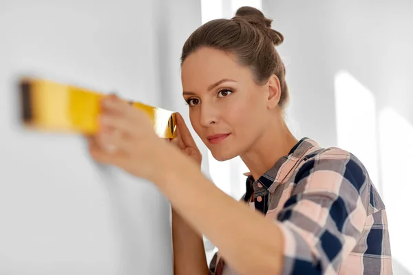 Woman with level measuring wall at home — Stockfoto