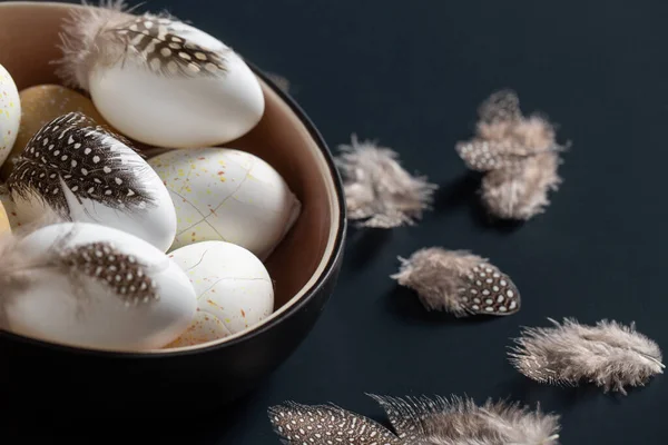 Påskägg med fjädrar i skålen på svart bord — Stockfoto