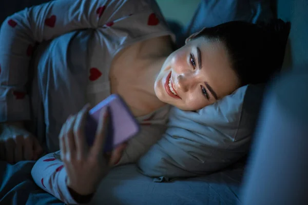 Tinédzser lány okostelefon feküdt az ágyban éjszaka — Stock Fotó