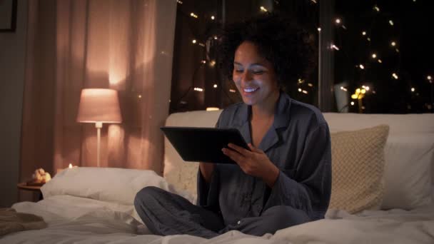 Lycklig kvinna med tablett dator sittande i sängen på natten — Stockvideo