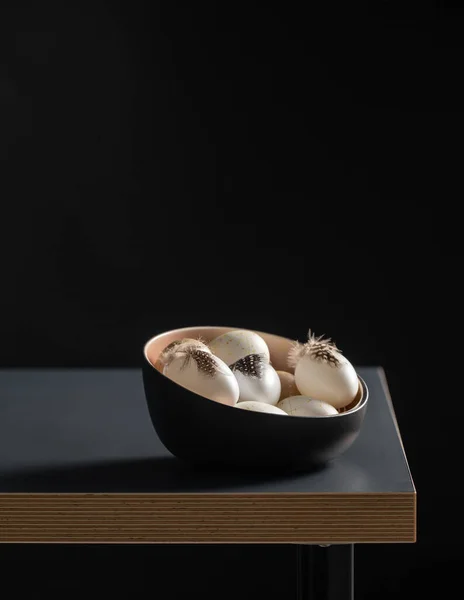 Huevos de Pascua con plumas en un tazón sobre una mesa negra — Foto de Stock