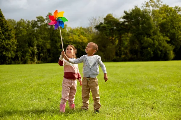 Crianças felizes brincando com pinwheel no parque — Fotografia de Stock