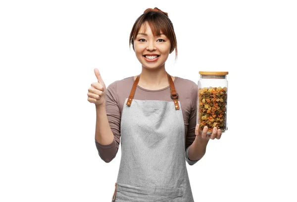Kvinna i förkläde med pasta i burk visar tummen upp — Stockfoto