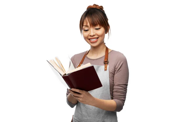 Улыбающаяся женщина в фартуке читает поваренную книгу — стоковое фото