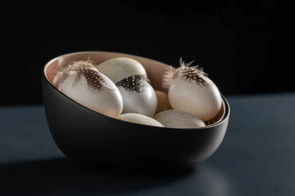 Ovos de Páscoa com penas na tigela na mesa preta — Fotografia de Stock