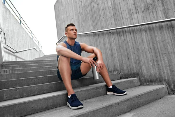 Tired sportsman with bottle sitting on stairs — Stock Photo, Image