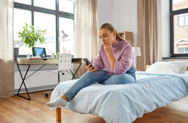 Menina triste com smartphone sentado na cama em casa — Fotografia de Stock