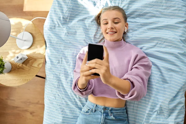 Lány fülhallgató okostelefon feküdt az ágyon — Stock Fotó