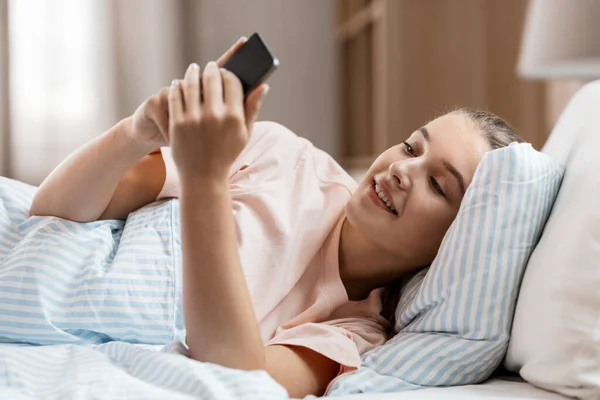 Glückliches Mädchen mit Smartphone zu Hause im Bett — Stockfoto