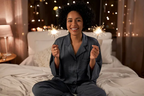 Femme heureuse avec des étincelles assis dans le lit la nuit — Photo