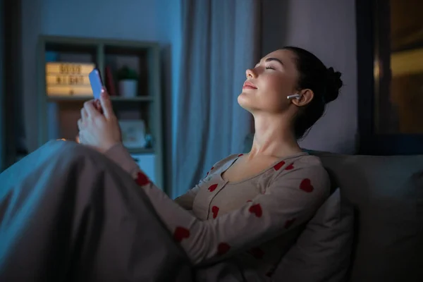 Gelukkig tiener meisje met telefoon en oortjes in bed — Stockfoto