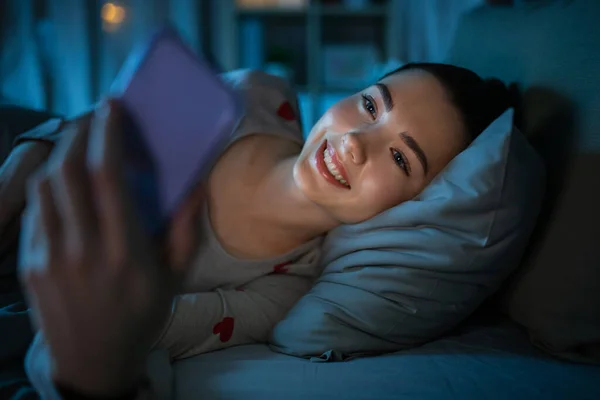 Adolescente con teléfono acostado en la cama por la noche — Foto de Stock