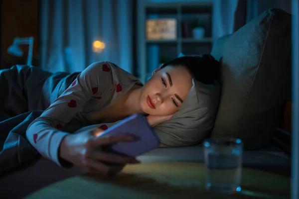 Gadis remaja dengan telepon berbaring di tempat tidur di malam hari — Stok Foto