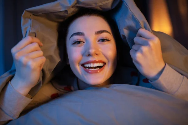 Glückliches Teenager-Mädchen liegt unter Decke im Bett — Stockfoto