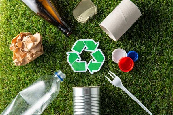 Letrero de reciclaje verde con residuos domésticos en hierba — Foto de Stock