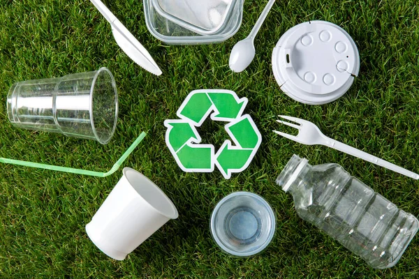 Green recycling sign and plastic waste on grass — Stock Photo, Image