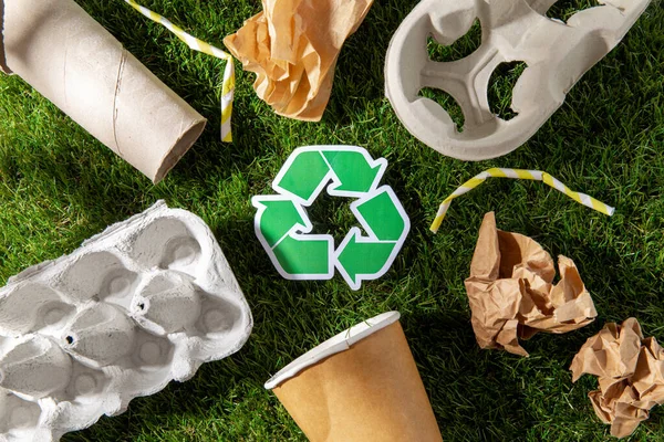 Green recycling sign and paper waste on grass — Stock Photo, Image