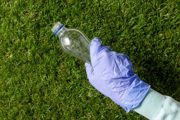 Mano nel guanto raccogliendo bottiglia di plastica da erba — Foto Stock