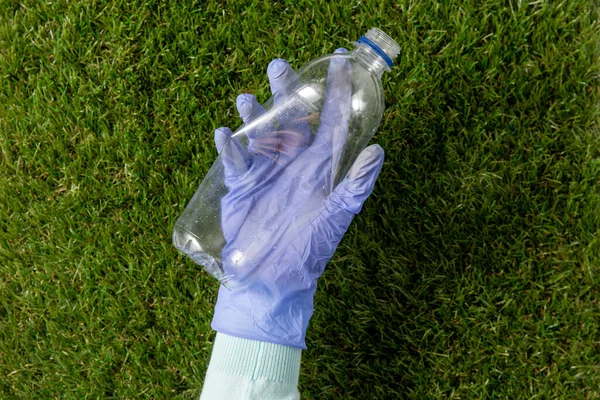 手拿着手套从草地上捡塑料瓶 — 图库照片