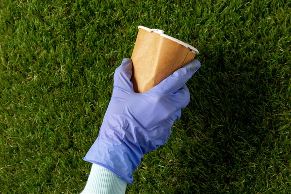 Κοντινό πλάνο του χεριού στο γάντι με φλιτζάνι καφέ στο γρασίδι — Φωτογραφία Αρχείου