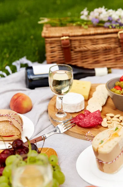 Comida, bebidas e cesta de piquenique em cobertor na grama — Fotografia de Stock