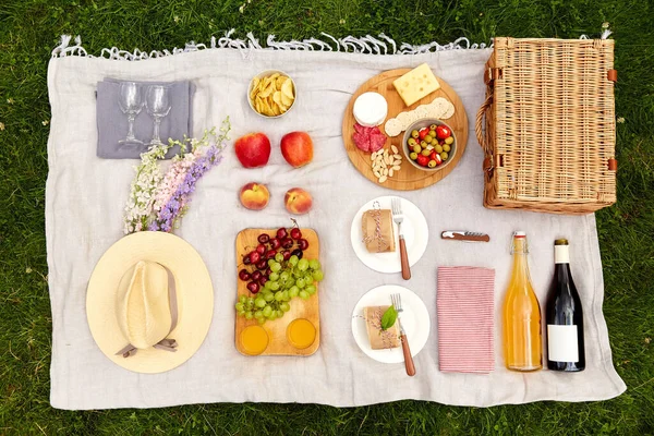 Comida, bebidas y cesta de picnic en manta sobre hierba — Foto de Stock