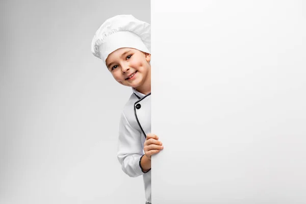 Šťastný malý chlapec v kuchaři toque s bílou deskou — Stock fotografie