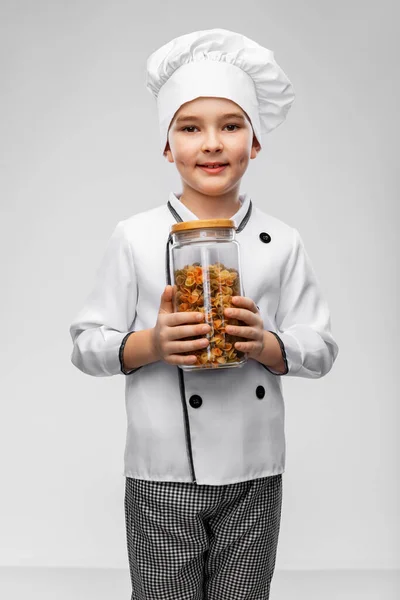 Menino sorridente em chefs toque segurando frasco com macarrão — Fotografia de Stock