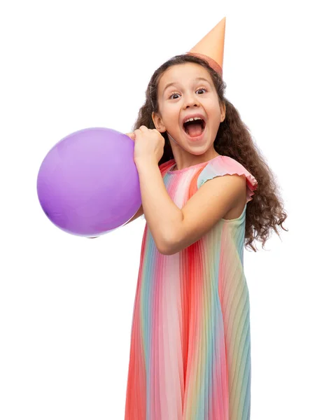 Menina engraçada no chapéu de festa de aniversário soprando balão — Fotografia de Stock