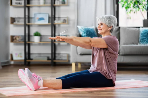 Mujer mayor sonriente haciendo ejercicio en la alfombra en casa — Foto de Stock