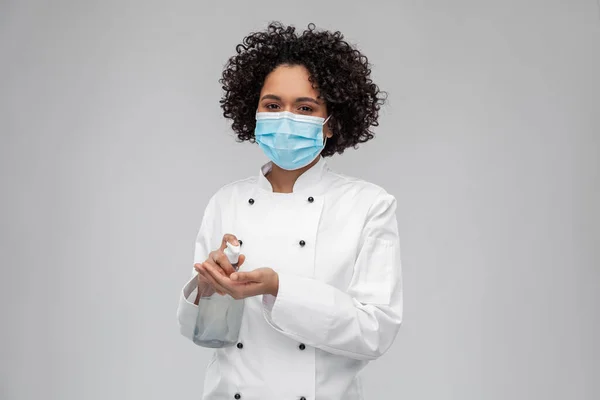 Female chef in mask using hand sanitizer or soap — Stockfoto