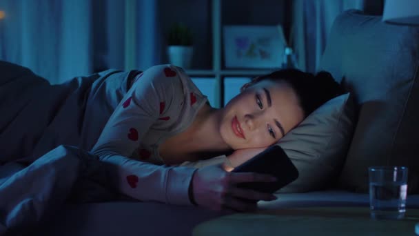 Adolescente em pijama com telefone na cama à noite — Vídeo de Stock