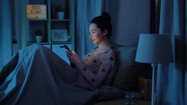 Tonårstjej i pyjamas med telefon i sängen på natten — Stockvideo