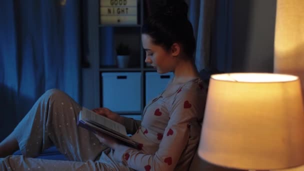 Дівчина-підліток читає книгу в ліжку вночі — стокове відео