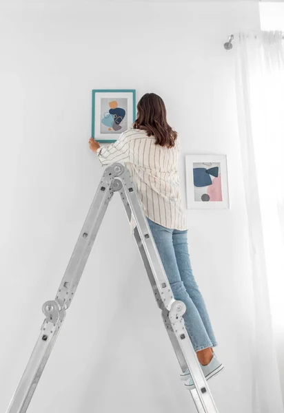 Mujer en escalera colgando imagen en marco en la pared —  Fotos de Stock